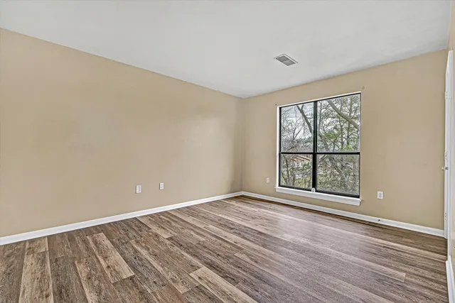 a view of an empty room with a window and wooden floor