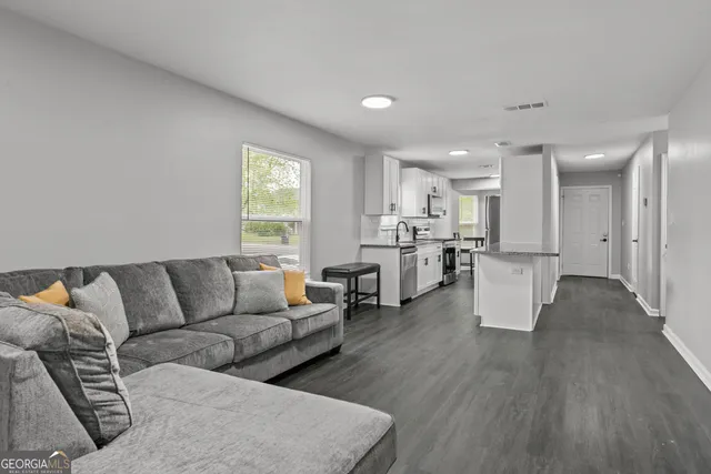 a living room with furniture and kitchen view with wooden floor