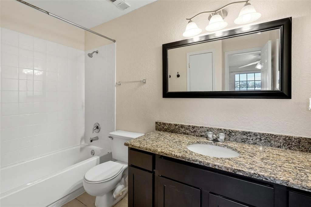 1039 South Hiawassee Road, Unit 2918 Orlando, FL 32835 - Photo 19 of 28 a bathroom with a granite countertop sink a toilet a mirror a vanity a bathtub and shower