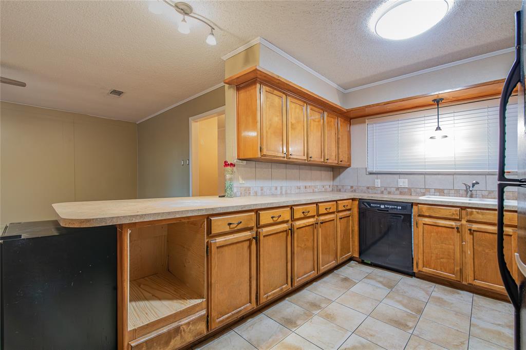 905 Martha Lane Azle, TX 76020 - Photo 4 of 18 Kitchen with brown cabinets, a peninsula, a textured ceiling, black appliances, and light countertops