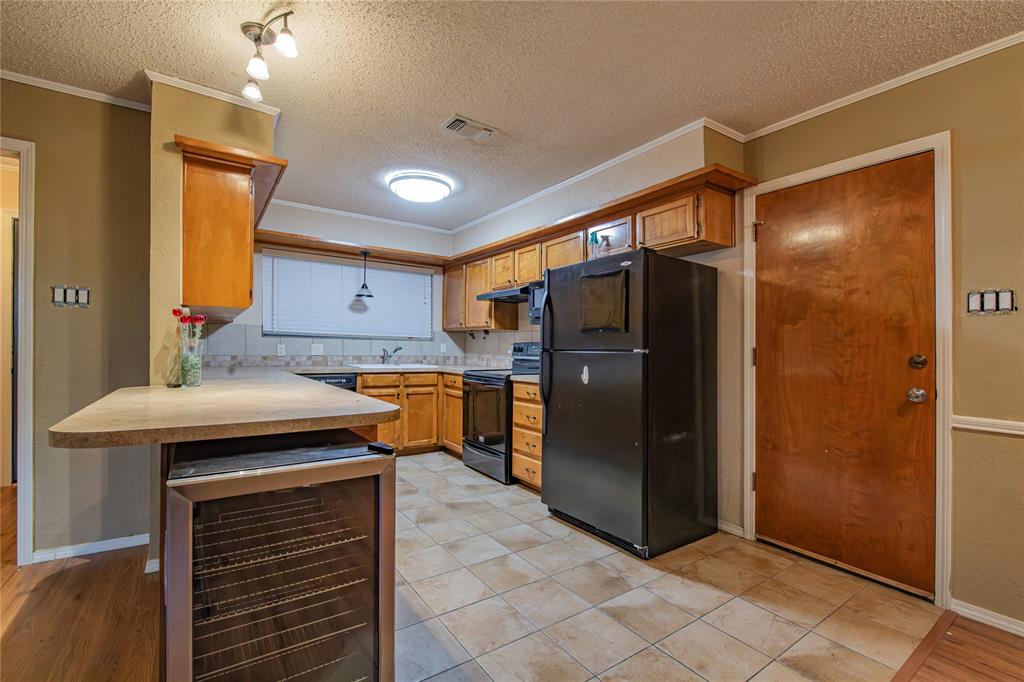 905 Martha Lane Azle, TX 76020 - Photo 5 of 18 Kitchen featuring a peninsula, light countertops, black appliances, beverage cooler, and brown cabinetry