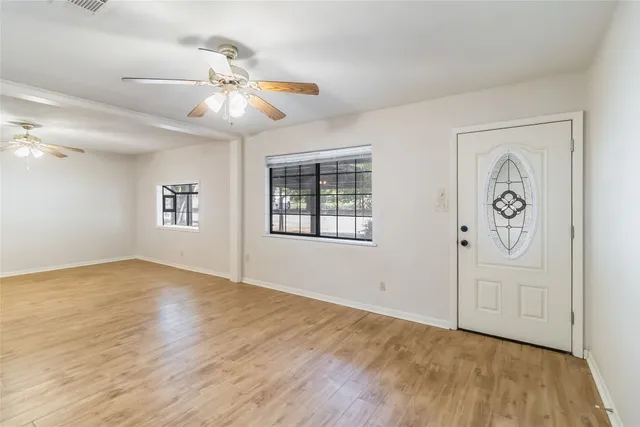 an empty room with wooden floor chandelier fan and windows