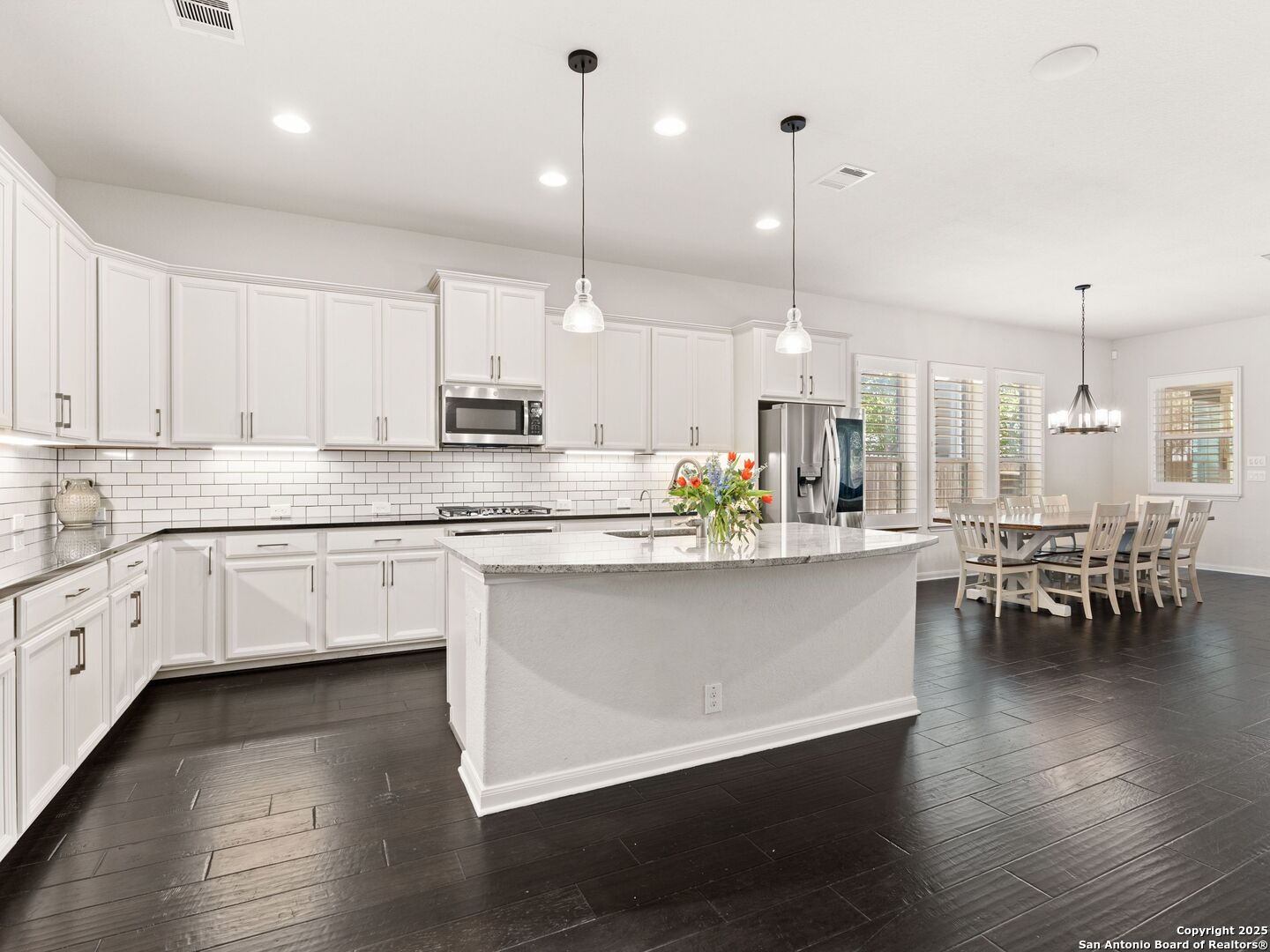 a kitchen with stainless steel appliances granite countertop a stove a sink dishwasher a refrigerator and white cabinets with wooden floor