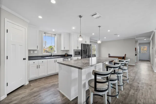a kitchen with a dining table chairs wooden floor cabinets and appliances