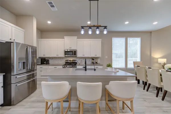 a kitchen with stainless steel appliances granite countertop a dining table chairs refrigerator and cabinets