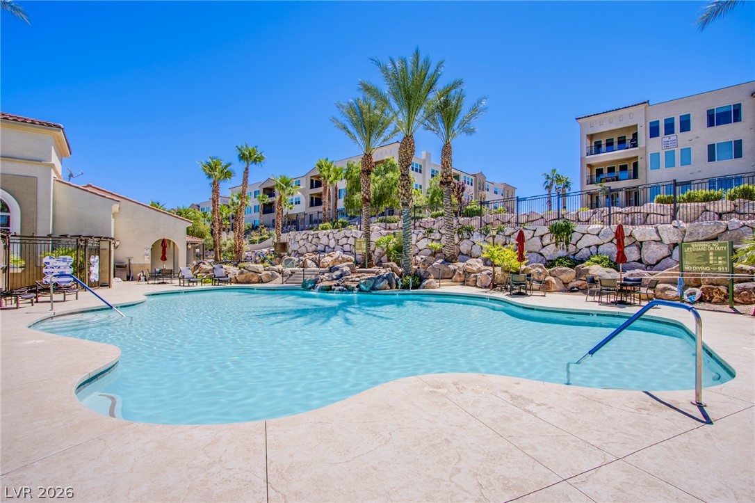 Palm trees and rock walls frame a sparkling resort-style swimming pool under clear blue skies.