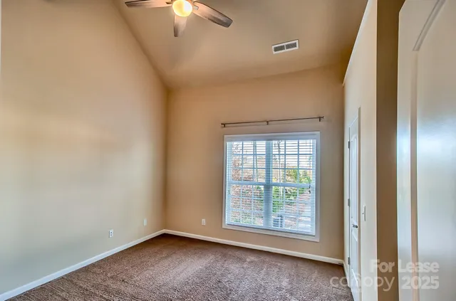 a view of an empty room with window and chandelier fan