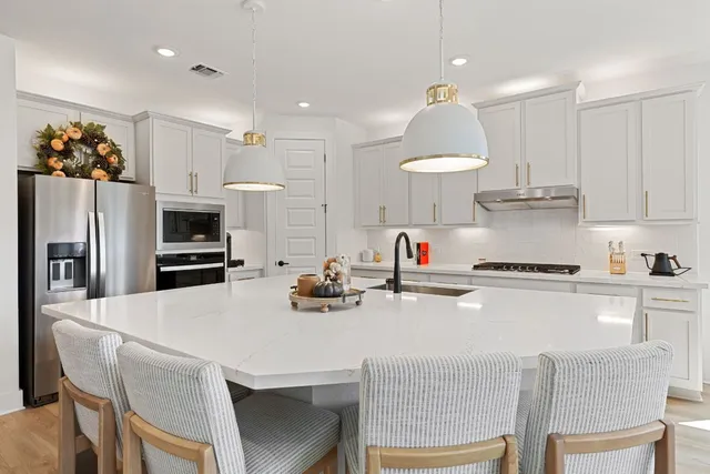 a kitchen with stainless steel appliances a sink dishwasher a stove and a dining table with wooden floor