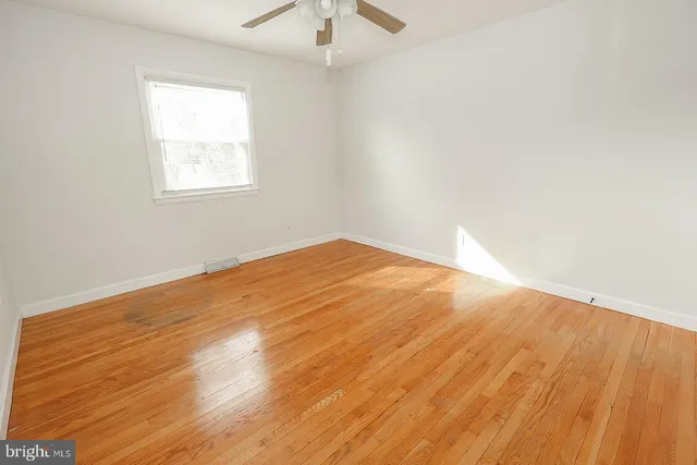 an empty room with wooden floor chandelier fan and windows