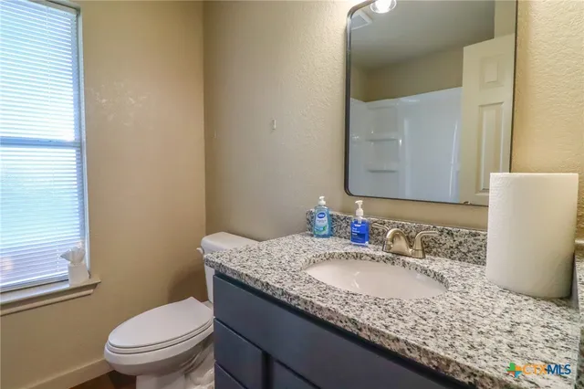 a bathroom with a granite countertop sink a toilet a mirror and shower