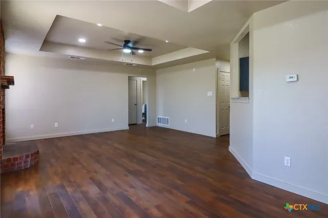 a view of an empty room with wooden floor and a ceiling fan