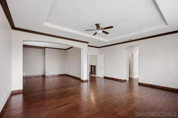 a view of an empty room with wooden floor and a ceiling fan