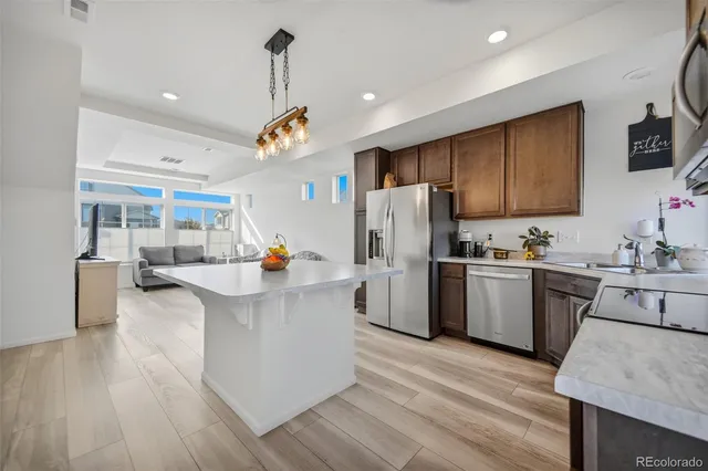 a kitchen with stainless steel appliances granite countertop a refrigerator a sink dishwasher a oven and a dining table with wooden floor