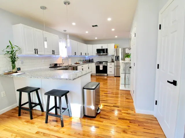 a kitchen with stainless steel appliances kitchen island granite countertop a stove a sink a refrigerator and white cabinets with wooden floor