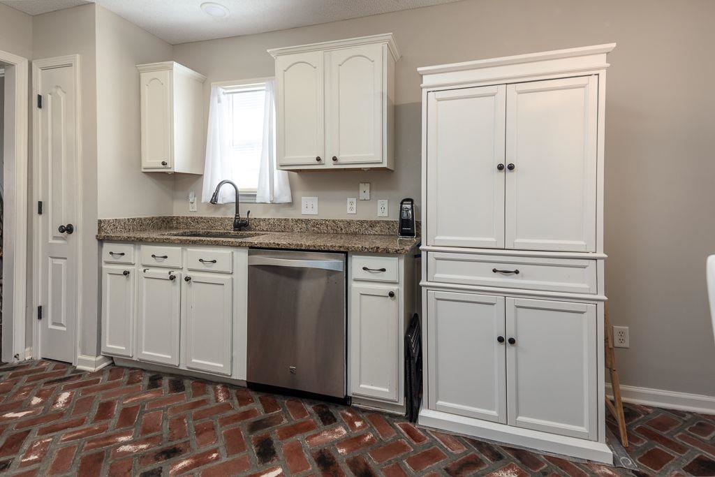 9768 Riggin Drive Memphis, TN 38002 - Photo 31 of 32 Kitchen featuring brick-finish flooring, white cabinetry with dark hardware, granite countertops, a stainless steel dishwasher, and a window with white drapes