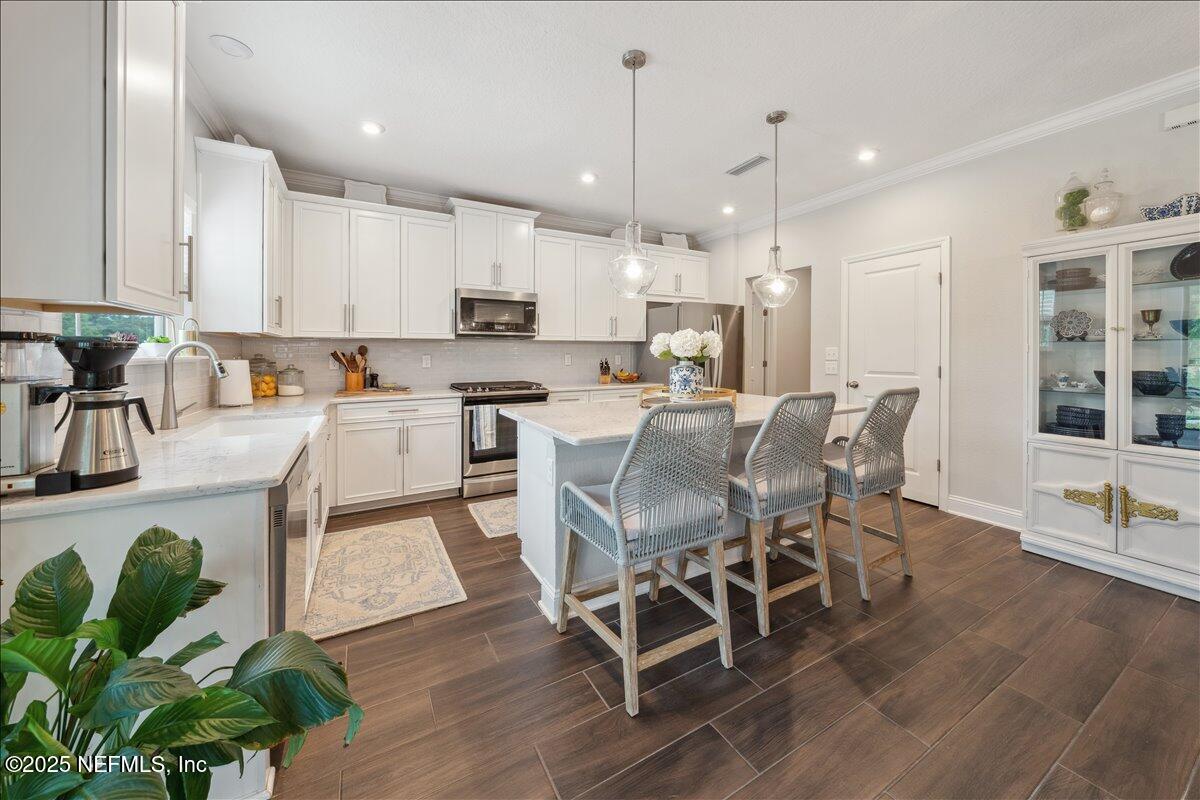 552 Meadow Creek Drive St. Johns, FL 32259 - Photo 8 of 62 a kitchen with stainless steel appliances granite countertop a stove top oven a sink a dining table and chairs with wooden floor