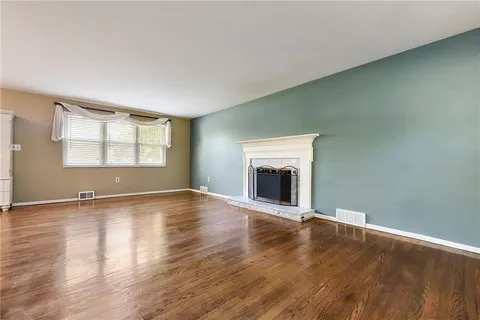 an empty room with wooden floor fireplace and windows