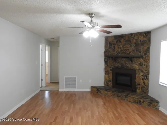 a view of an empty room with wooden floor fireplace and a window