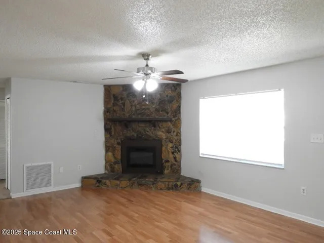 a view of an empty room with wooden floor fireplace and a window