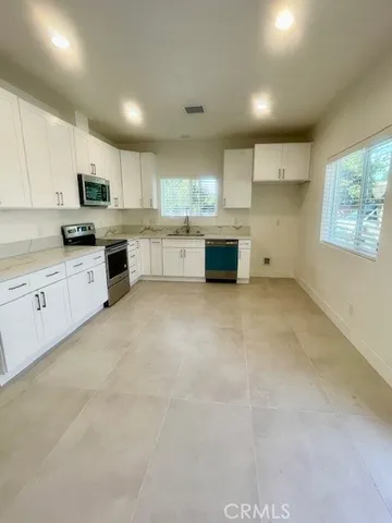 a large kitchen with stainless steel appliances granite countertop a stove a sink a refrigerator and white cabinets with wooden floor