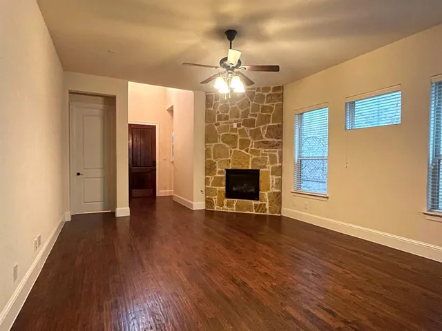 a view of an empty room with wooden floor fireplace and a window