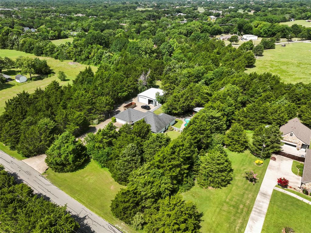401 Rugged Drive Red Oak, TX 75154 - Photo 39 of 40 Expansive wooded property featuring a residential structure with a dark roof, a detached auxiliary building with a light-colored roof, and an in-ground swimming pool