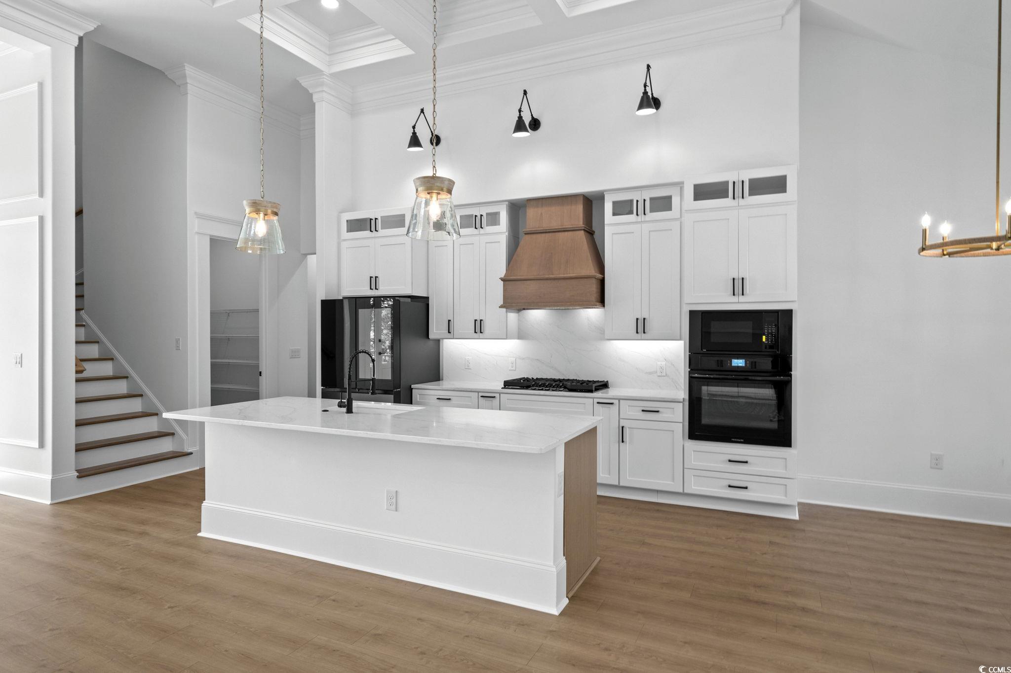 9282 Checkerberry Square Calabash, NC 28467 - Photo 8 of 40 Kitchen with a high ceiling, hanging light fixtures, white cabinetry, coffered ceiling, and glass insert cabinets