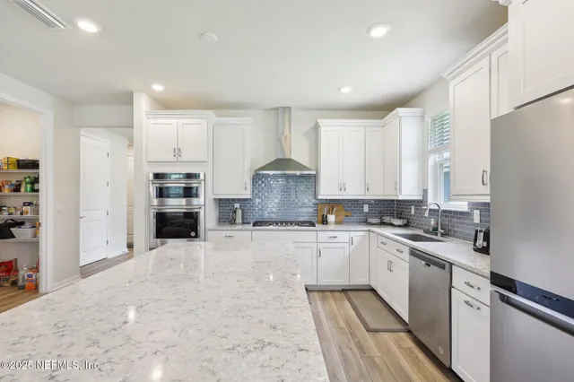 a kitchen with stainless steel appliances granite countertop a stove top oven a sink and white cabinets