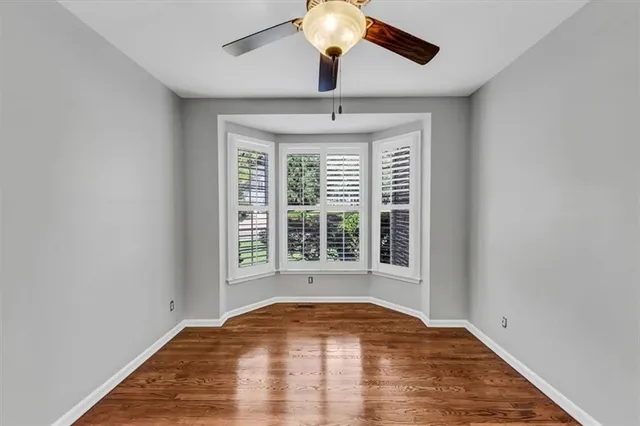 a view of an empty room with wooden floor and a ceiling fan