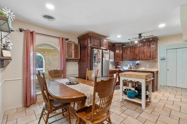 a kitchen with stainless steel appliances granite countertop a stove a refrigerator a sink a dining table and chairs