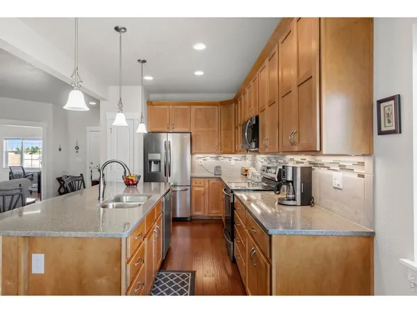 a kitchen with stainless steel appliances kitchen island granite countertop a stove a sink a microwave a dining table and chairs with wooden floor