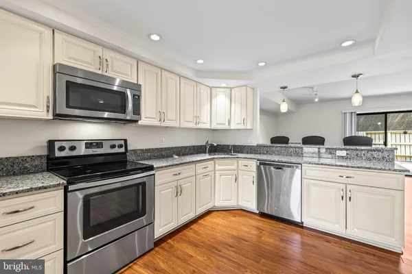 a kitchen with stainless steel appliances granite countertop a stove top oven a sink dishwasher and white cabinets with wooden floor