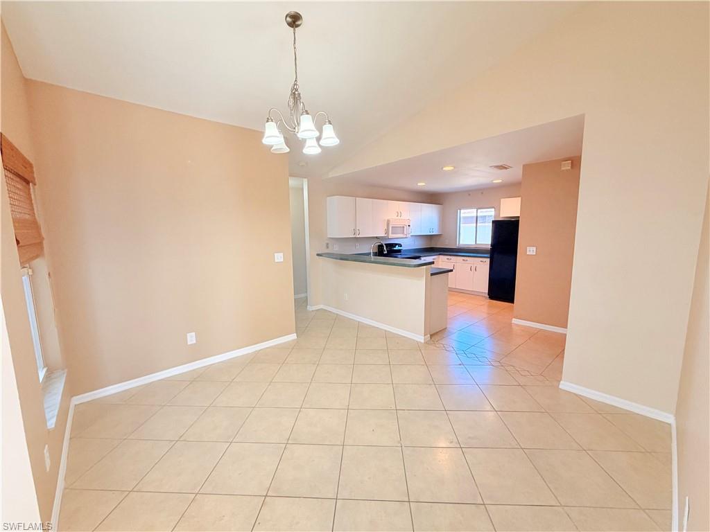 8397 Bahamas Road Fort Myers, FL 33967 - Photo 7 of 37 Kitchen with dark countertops, a peninsula, light tile patterned flooring, a chandelier, and freestanding refrigerator