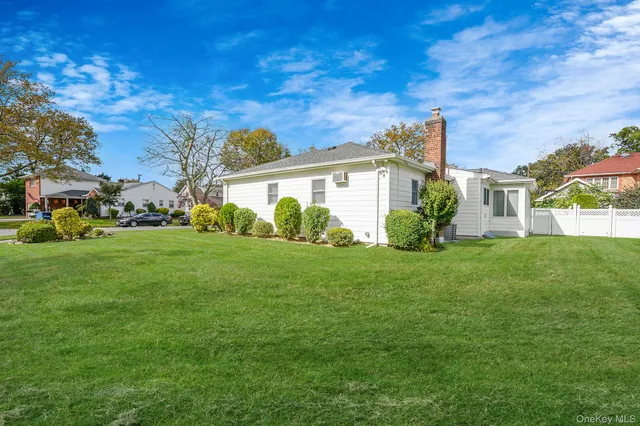 a view of a white house in front of a big yard with plants and large trees