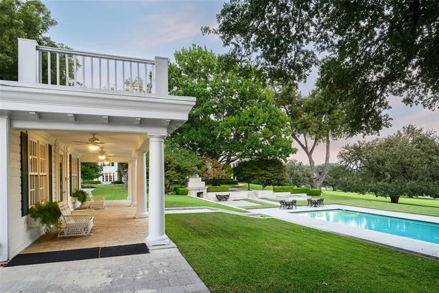 a view of swimming pool with lawn chairs and large trees