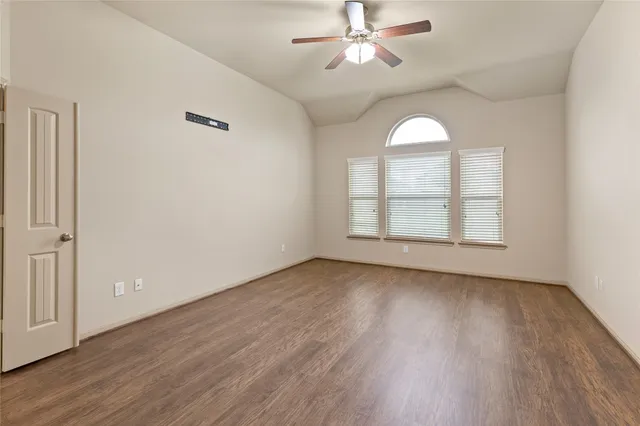 an empty room with wooden floor fan and windows