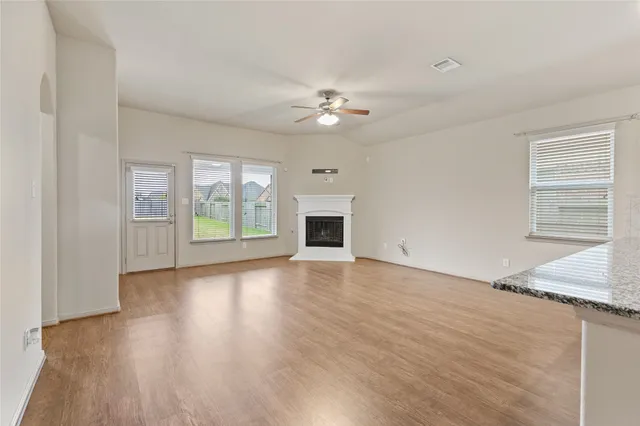 an empty room with wooden floor a ceiling fan and windows
