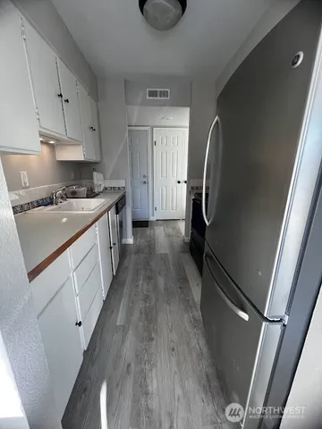 a kitchen with granite countertop a refrigerator a sink dishwasher a stove and white countertops with wooden floor