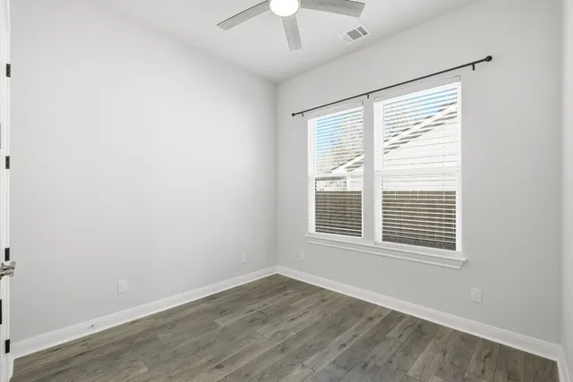 a view of an empty room with wooden floor and a chandelier fan