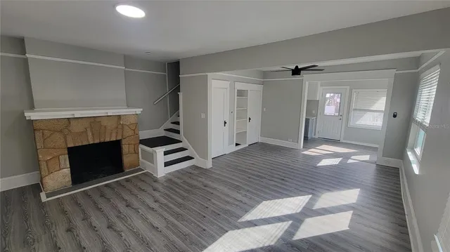 a view of an empty room with wooden floor fireplace and a window