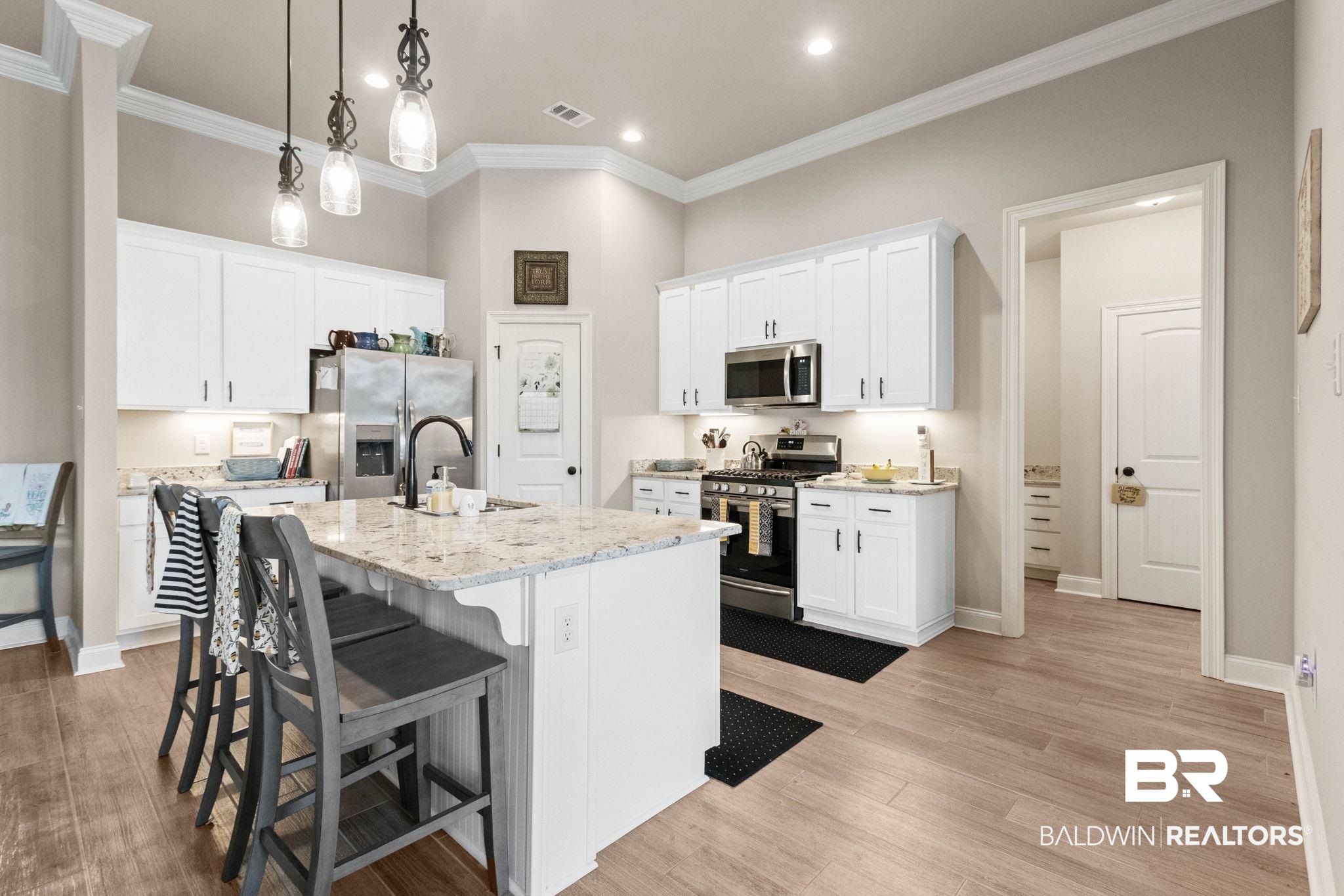 22244 Hibiscus Circle Foley, AL 36535 - Photo 20 of 51 Kitchen featuring a central island with countertop seating, white cabinetry, integrated stainless steel appliances, and wood-finish flooring