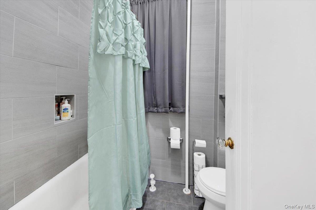 2312 Morgan Avenue Bronx, NY 10469 - Photo 12 of 36 Full bathroom featuring tile walls, shower / bathtub combination with curtain, and dark tile patterned floors