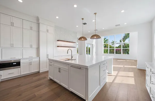 a large kitchen with kitchen island granite countertop a stove a sink a refrigerator and white cabinets with wooden floor