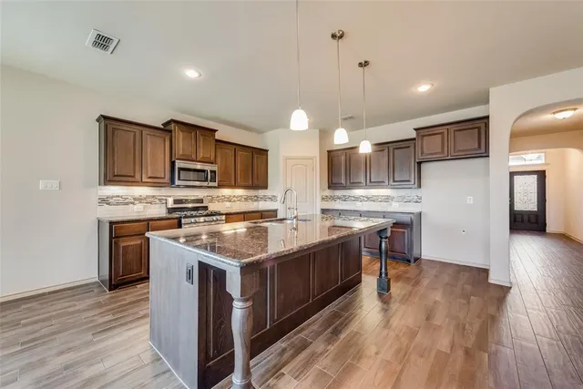 a kitchen with stainless steel appliances granite countertop a stove a sink dishwasher a refrigerator and a oven with wooden floor