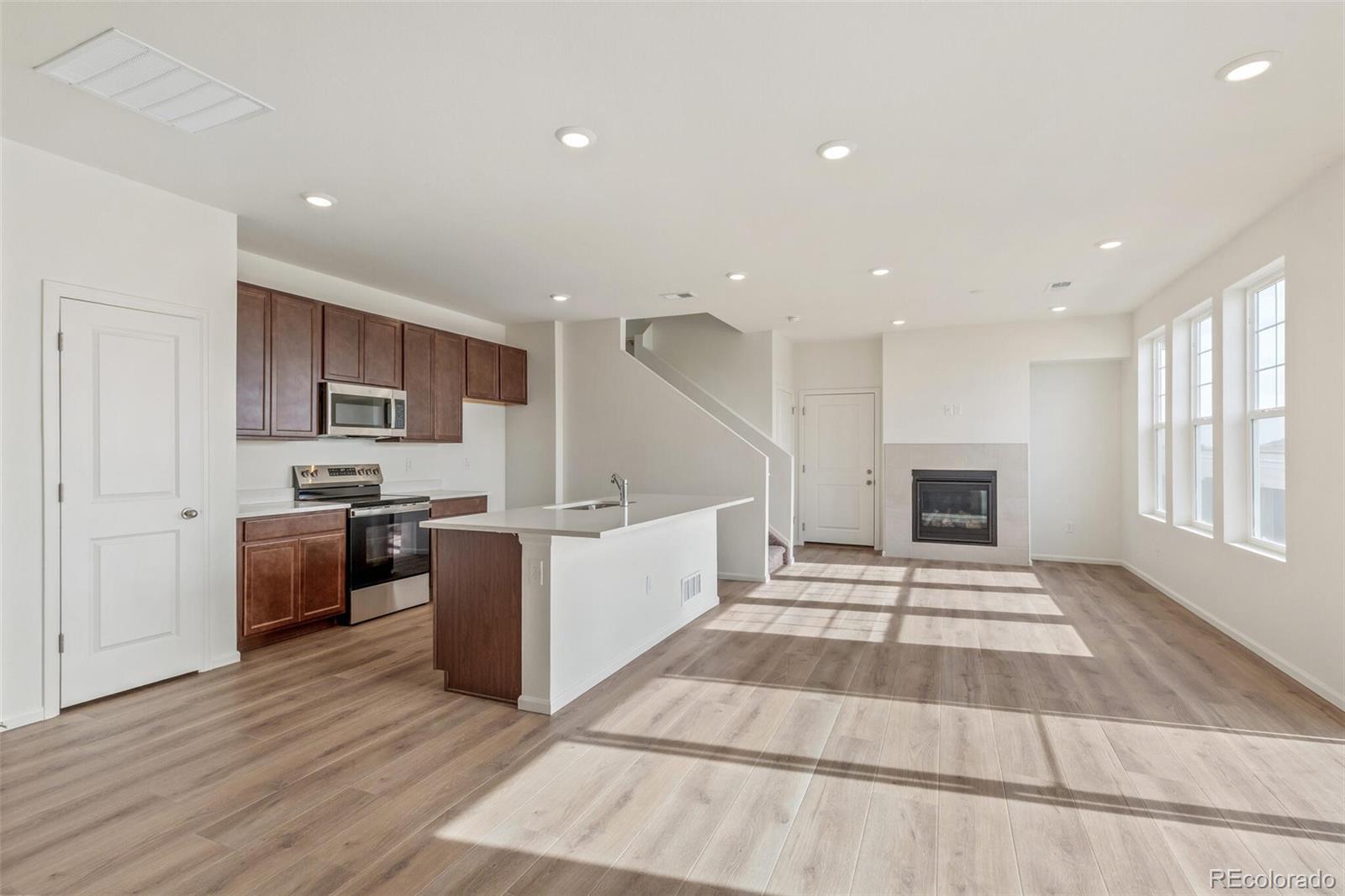 28636 East 6th Place Watkins, CO 80137 - Photo 2 of 32 a large white kitchen with kitchen island a sink wooden floor and stainless steel appliances