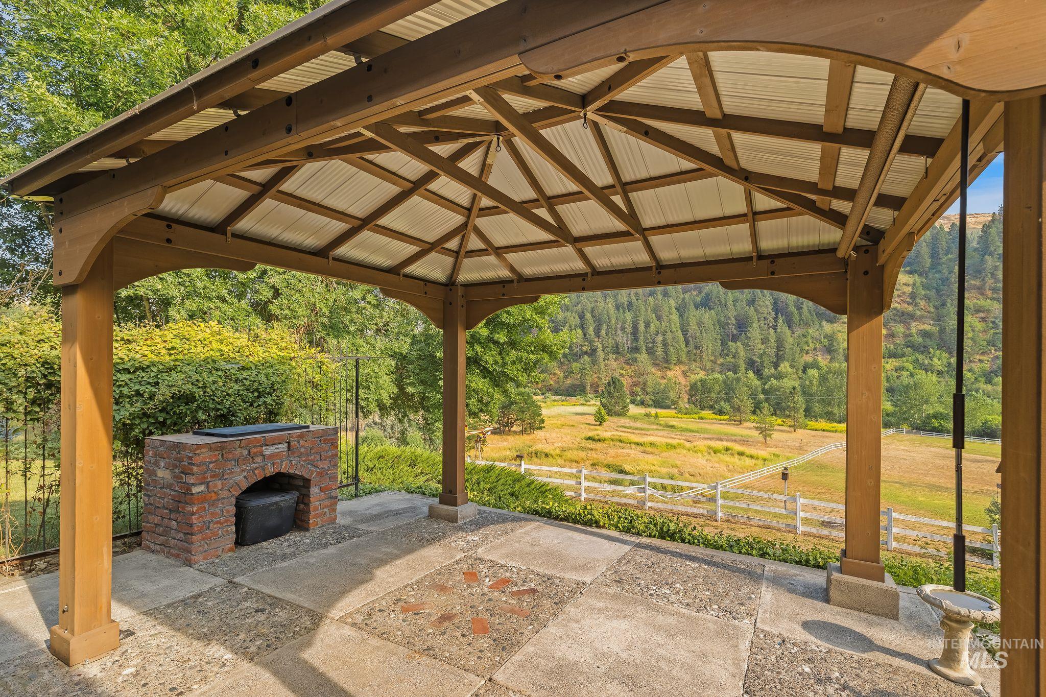 1091 Cedar Ridge Road Kendrick, ID 83537 - Photo 31 of 48 Covered outdoor entertaining space featuring a substantial wood-beam pergola with polycarbonate paneling, brick wood-fired oven, concrete patio flooring, and panoramic mountain and valley backdrop