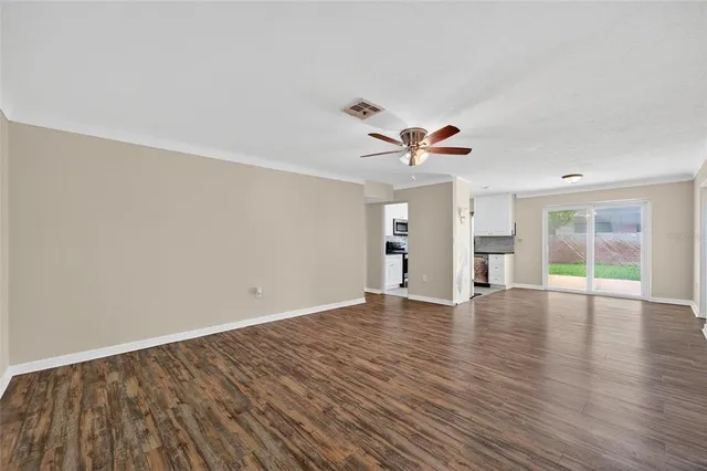 an empty room with wooden floor ceiling fan and windows
