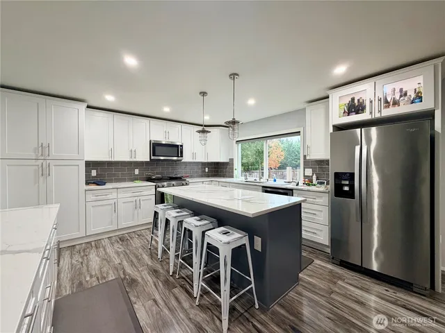 a kitchen with stainless steel appliances granite countertop a refrigerator a sink dishwasher a stove and white countertops with wooden floor