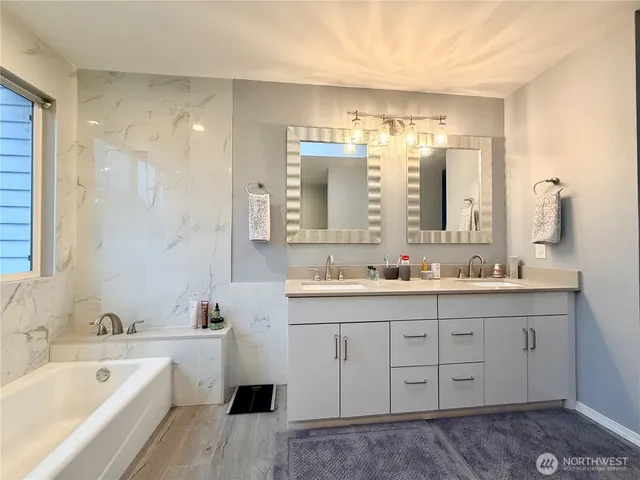 a bathroom with a tub a sink double vanity and mirror