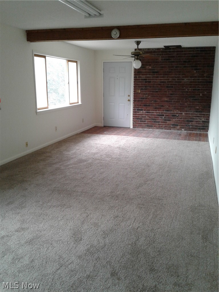 613 Jackson Street Amherst, OH 44001 - Photo 13 of 29 Living room featuring beam ceiling, brick wall, light colored new carpet, and a ceiling fan